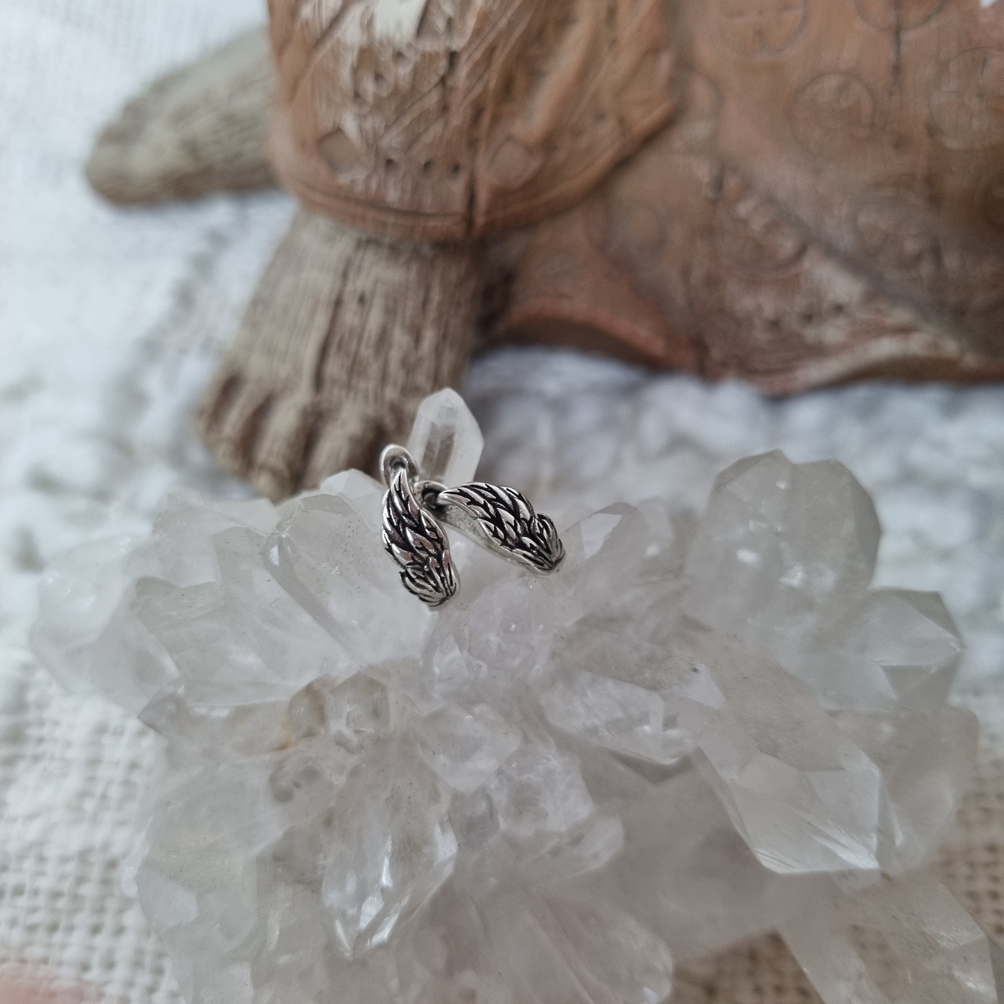 Close-up of angel wing earrings resting on clear quartz crystal.