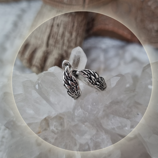 Close-up of angel wing earrings resting on clear quartz crystal.