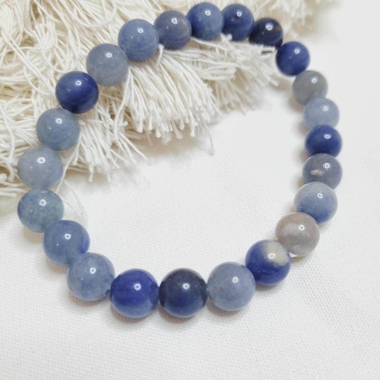 Beaded bracelet with blue and gray beads on a white fabric background.Natural Blue Aventurine