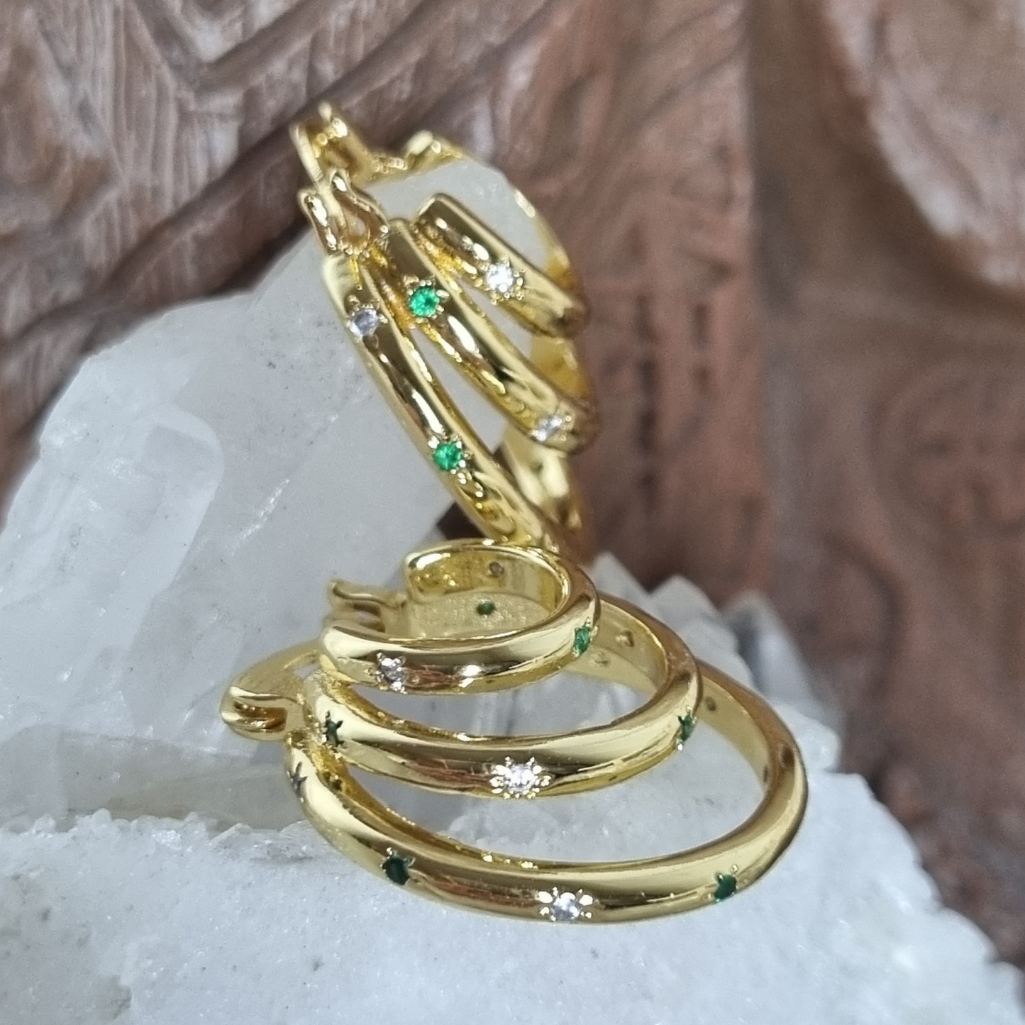 Pair of stacked hoop earrings with emerald and clear cubic zirconia stones, photographed lying flat on a neutral background.
