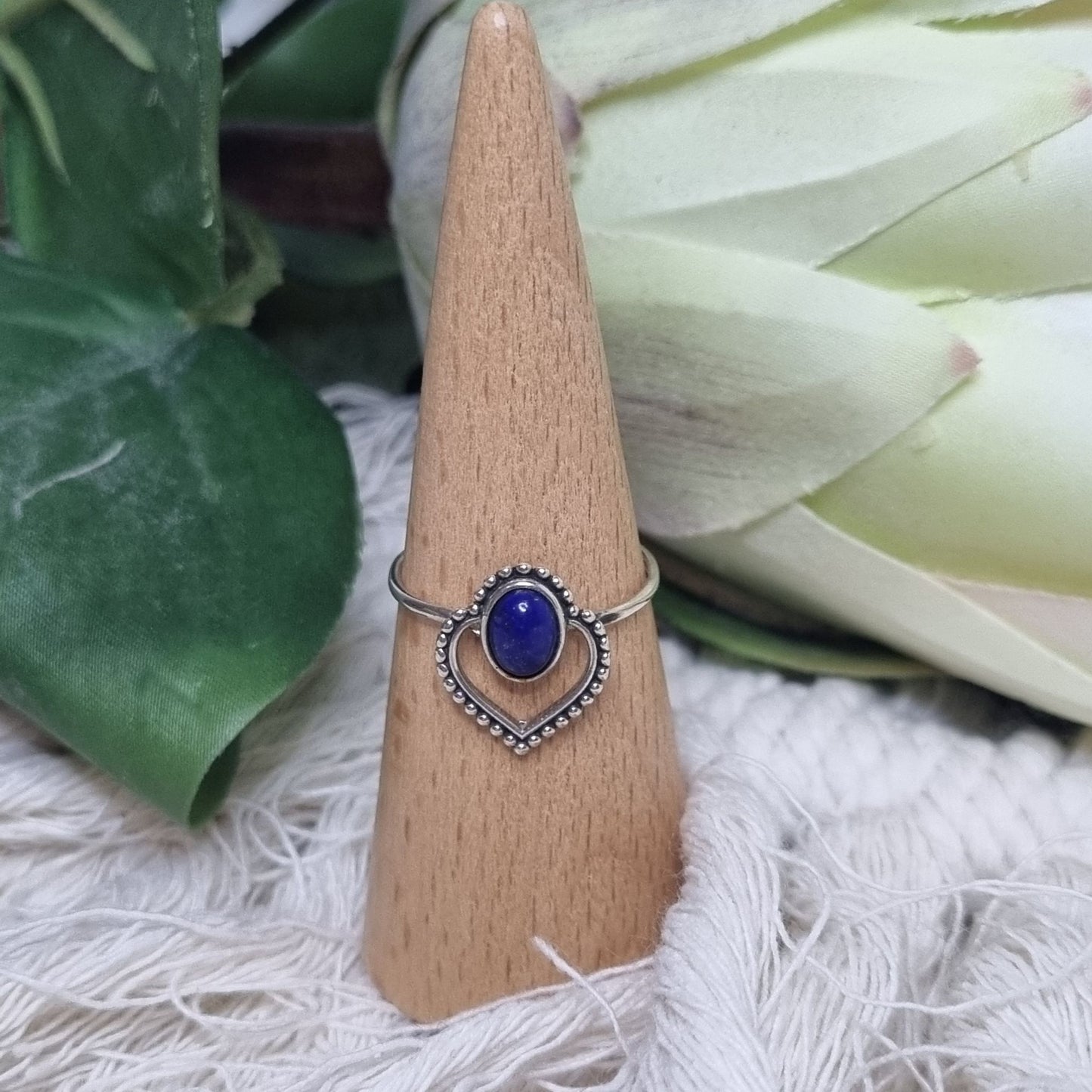 Front view of sterling silver ring featuring oval lapis lazuli stone set in a beaded heart frame