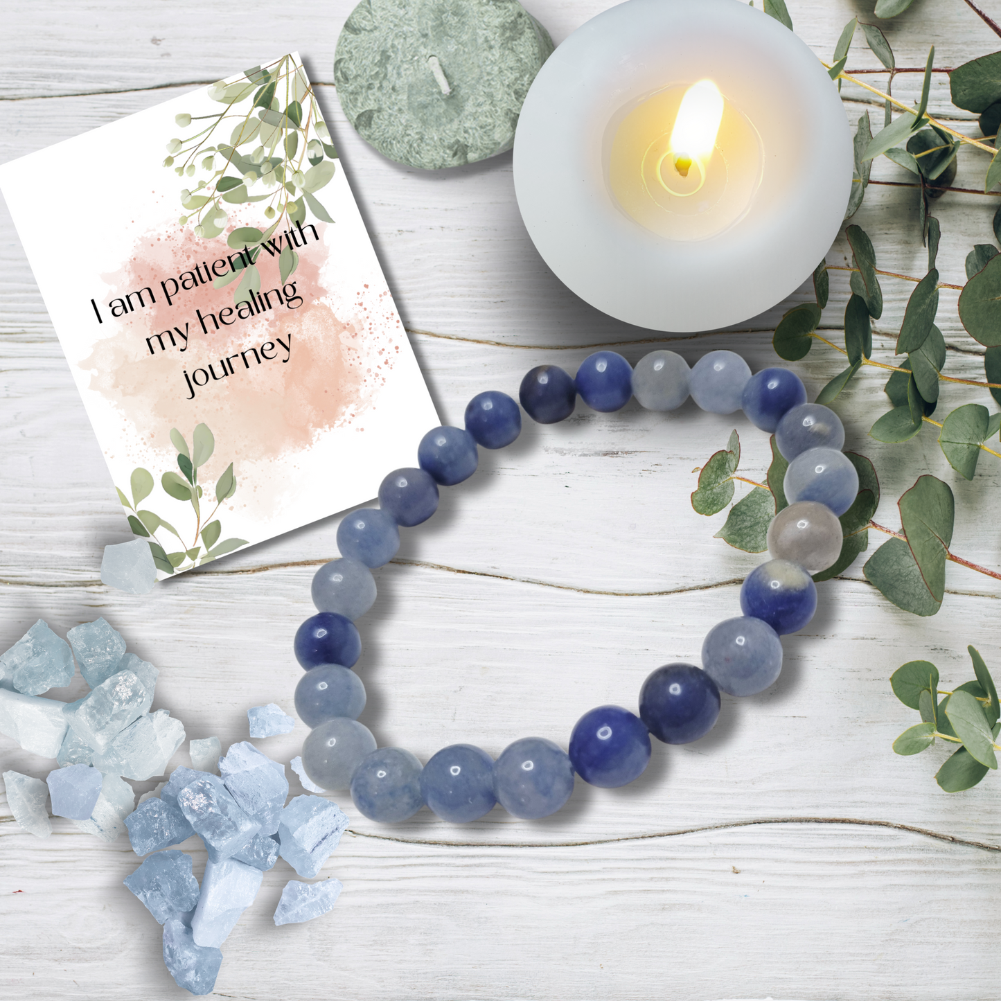 Blue and gray beaded bracelet on a white wooden surface with a lit candle and card.Step into quiet confidence with our Blue Aventurine Tumblestone Bracelet,
