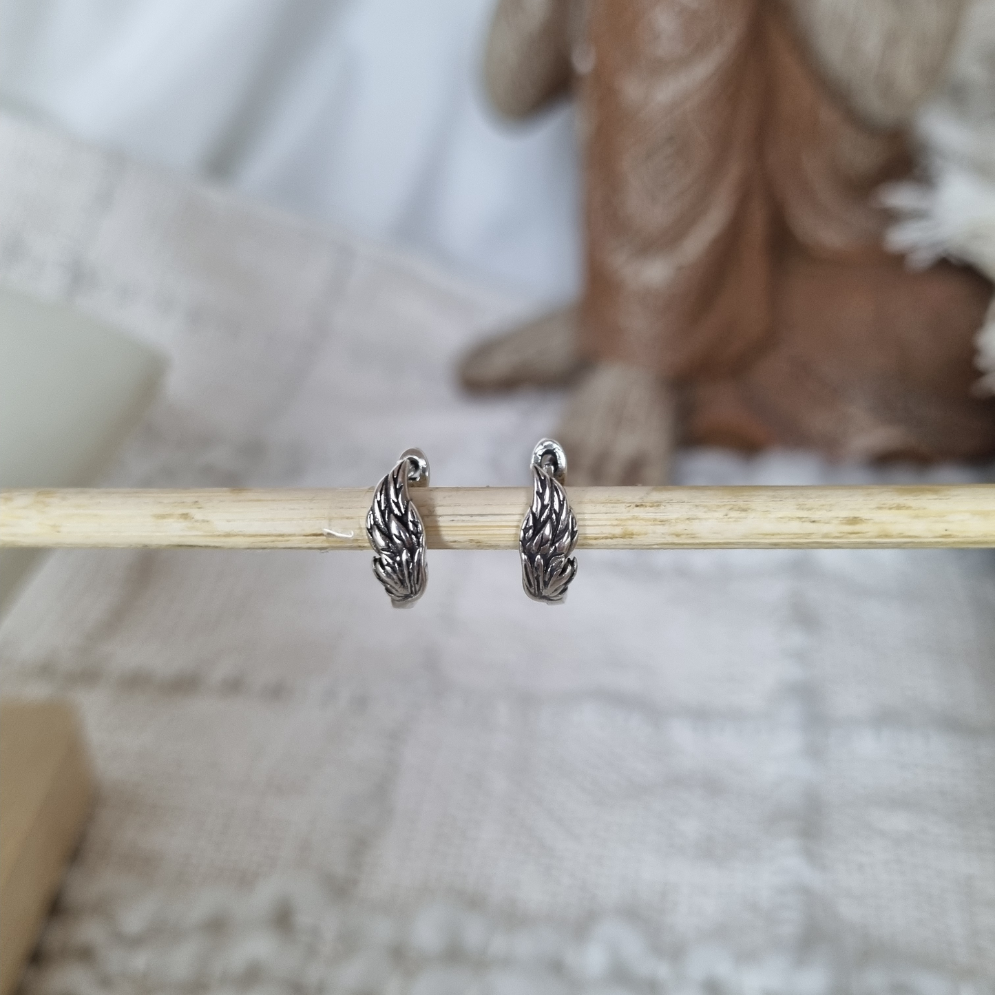 Sterling silver angel wing hoop earrings displayed on wooden rod.