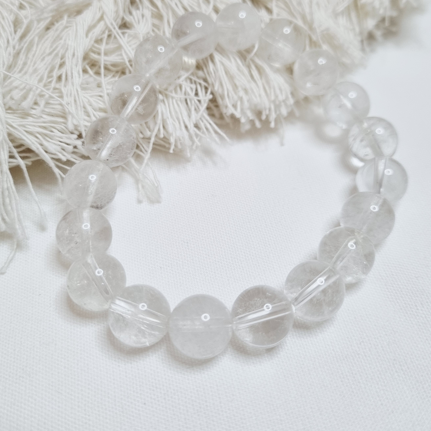 Clear beaded bracelet on a white background with decorative elements. as the “Master Healer,” Clear Quartz is believed to amplify energy,
