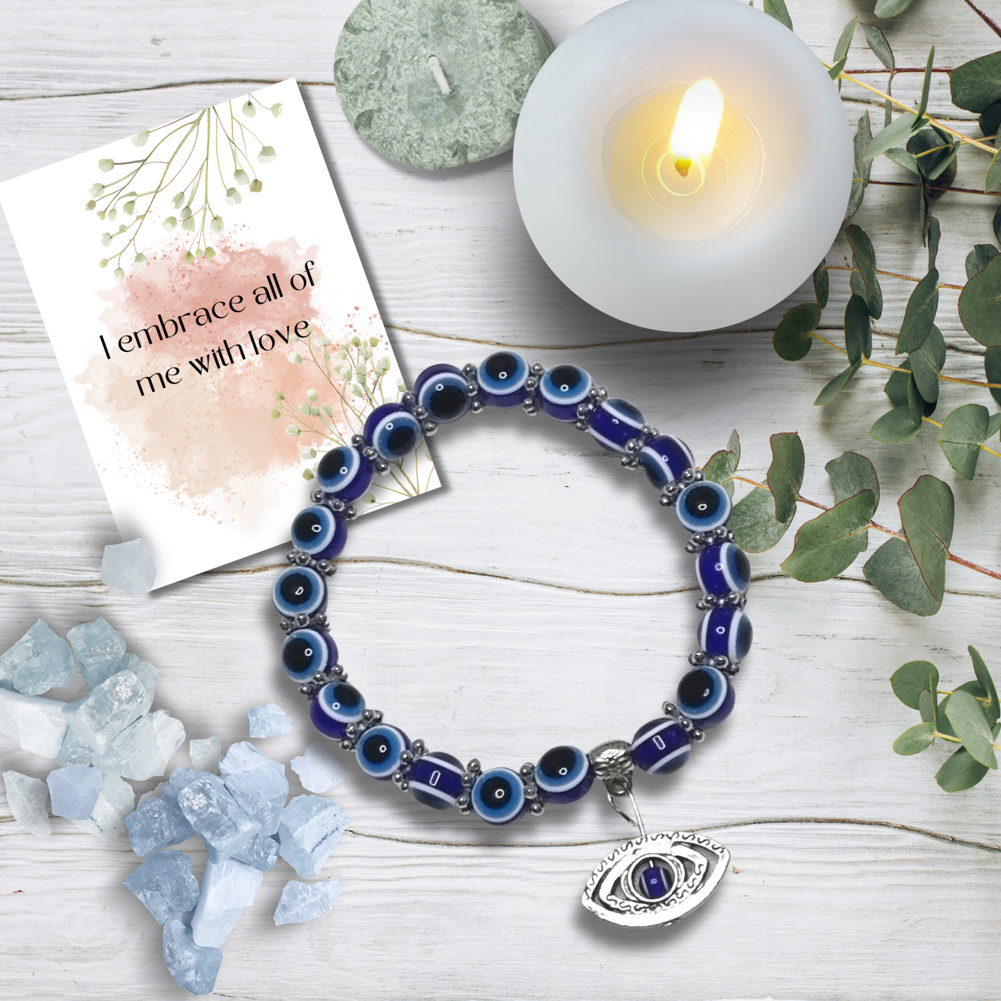 Blue beaded bracelet with evil eye charm on a wooden surface with a candle and card.