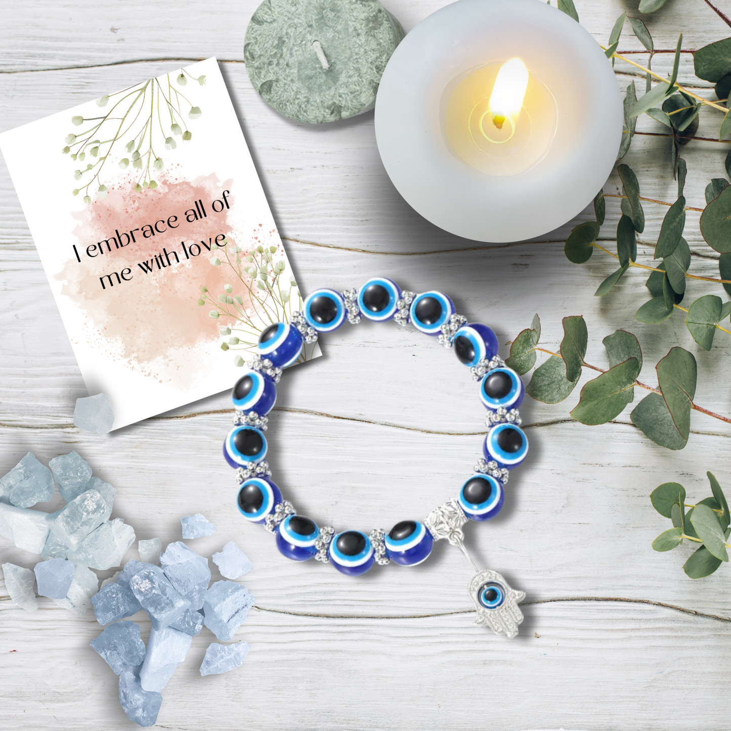 Evil eye bracelet with a candle, card, and crystals on a wooden surface