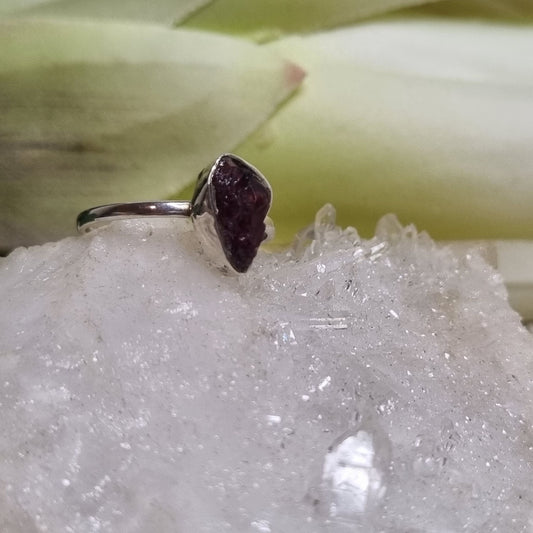 Silver ring with a purple stone on a crystal surface with a blurred natural background