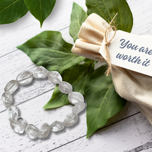 Clear beaded bracelet with a beige fabric pouch and tag on green leaves
