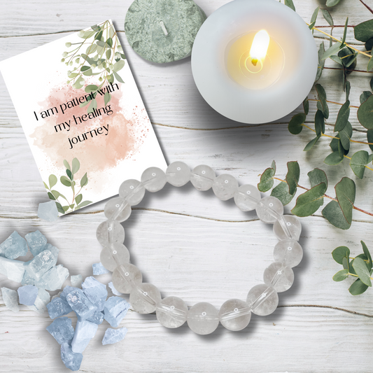 Crystal bracelet, card, and candle on a wooden surface with greenery