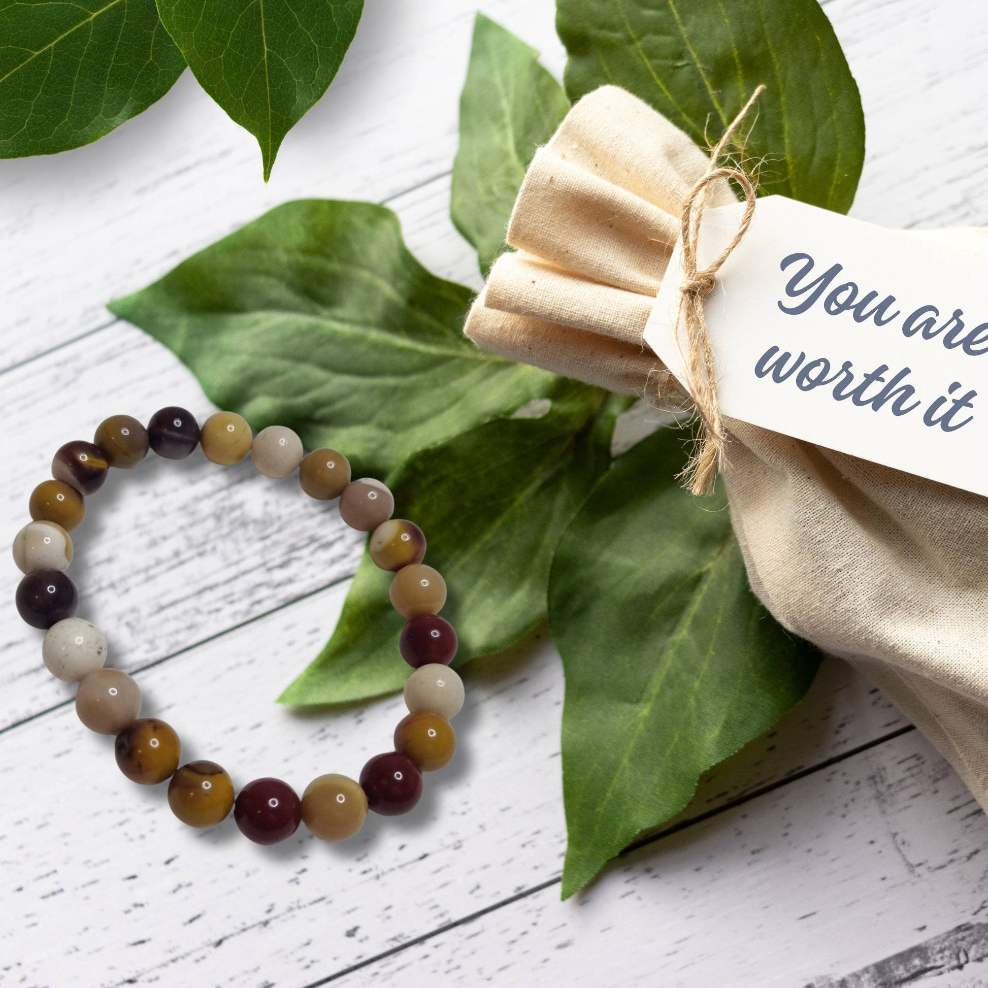 Beaded bracelet on a white wooden surface with green leaves and a tag reading 'You are worth it'.