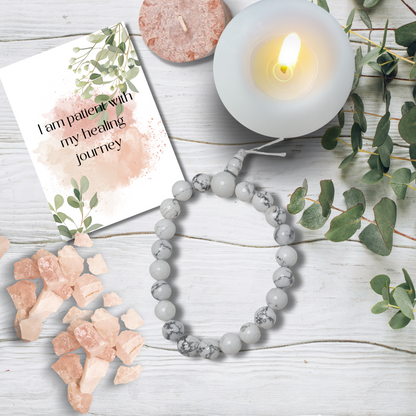 Gray beaded bracelet on a wooden surface with a candle, card, and crystals.White Howlite Tumblestone Bracelet