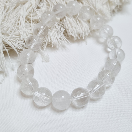 Clear beaded bracelet on a white background with decorative elements. as the “Master Healer,” Clear Quartz is believed to amplify energy,