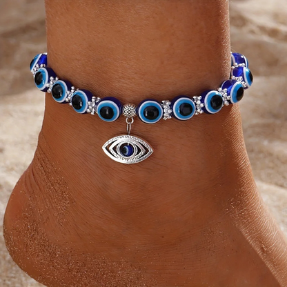 Anklet with blue and black eye-shaped beads on a sandy background