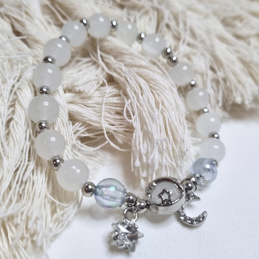 Bracelet with white opal beads and silver moon and star charms on a textured white background
